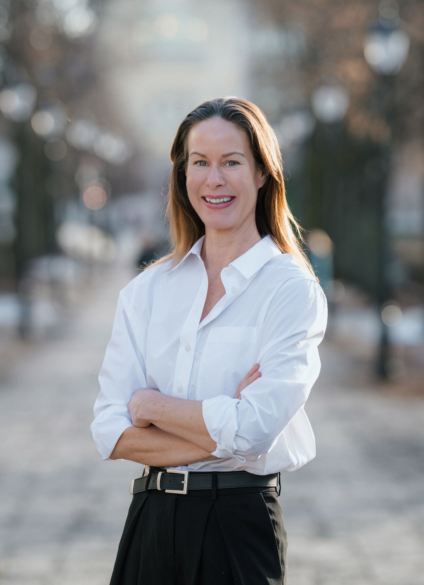 Maria smiler og står med armene i kors utendørs, iført hvit skjorte og mørke bukser